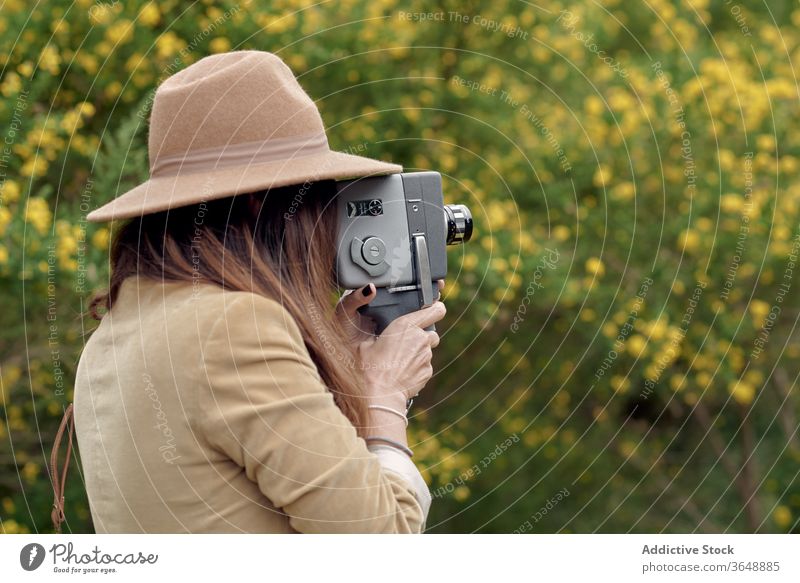 Fotograf, der mit einer alten Videokamera im Garten Videoaufnahmen macht Aufzeichnen Fotokamera Augen geschlossen Blütezeit Blume Baum Park Ast fokussiert