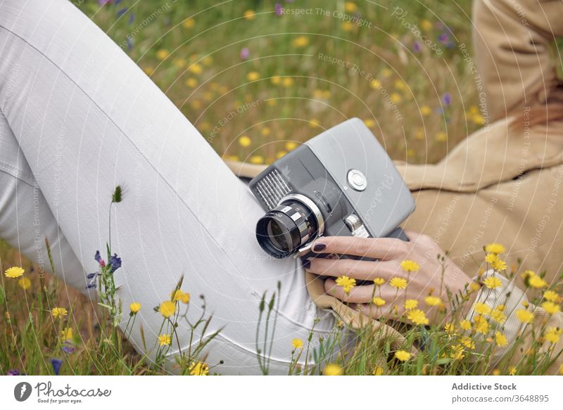Gesichtslose, auf Gras ruhende Frau mit Retro-Videokamera Fotokamera Hut elegant Wiese Deckblatt Blume Landschaft altehrwürdig Lügen Tierhaut Fotograf retro