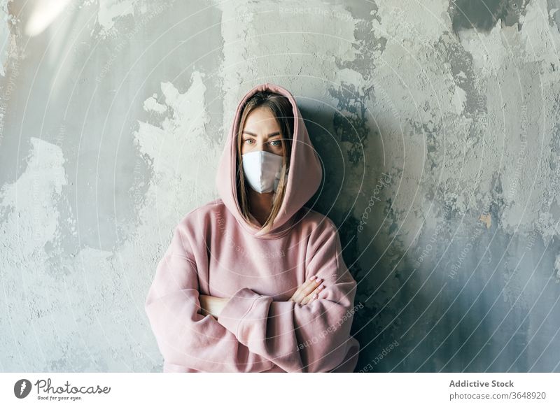 Frau mit steriler Maske steht während der Quarantänezeit in Wandnähe Mundschutz Selbstisolierung Unzufriedenheit Coronavirus zu Hause Beton heimisch