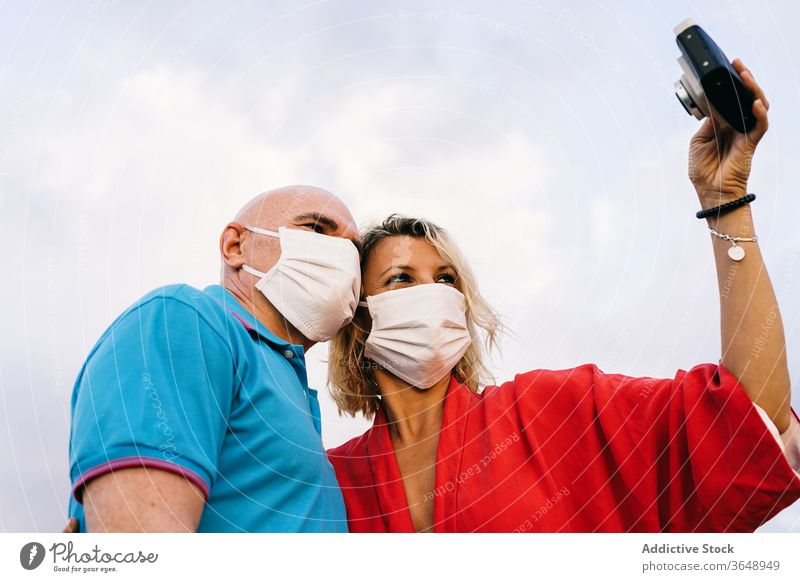 Glückliches Paar mit Atemschutzmasken, das sich am Smartphone selbstständig macht Selfie Mundschutz bezaubernd Coronavirus Sommer Inhalt Handy benutzend Telefon