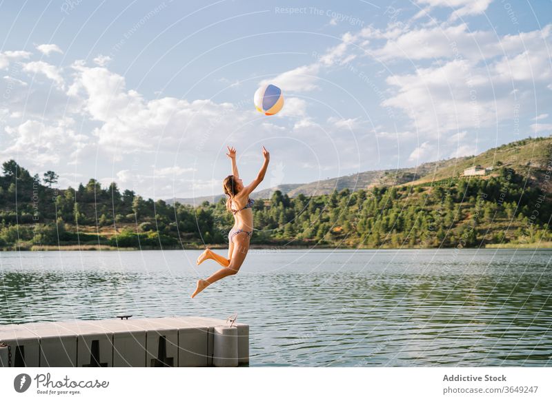Verspieltes Teenager-Mädchen springt vom Pier in den See Beachball spielen springen Teich Sommer Feiertag Urlaub genießen aufblasbar Gummi Bikini Wasser