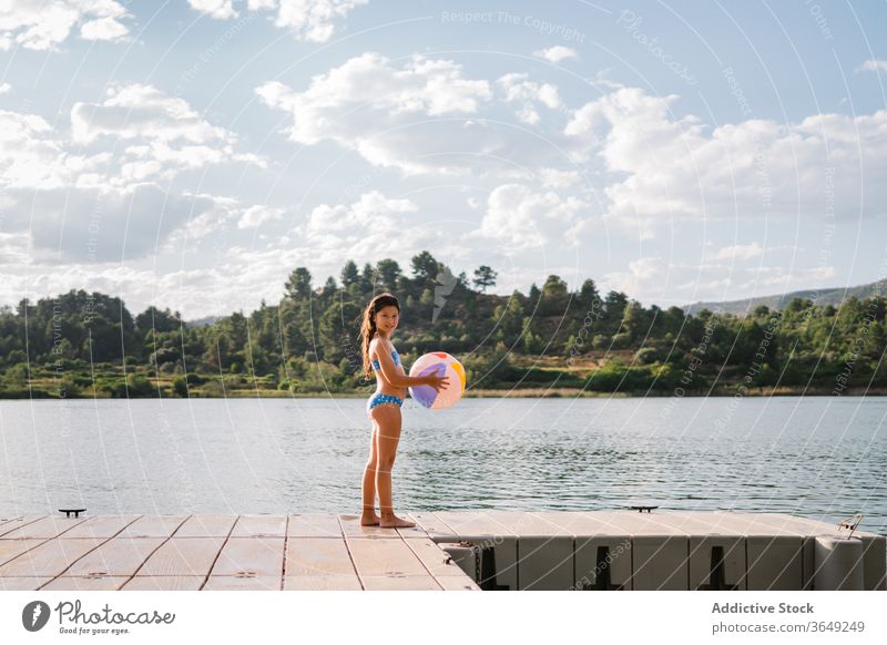 Verspieltes kleines Mädchen steht am Pier am See Beachball spielen Teich Sommer Feiertag Urlaub genießen aufblasbar Gummi Kind Bikini Wasser