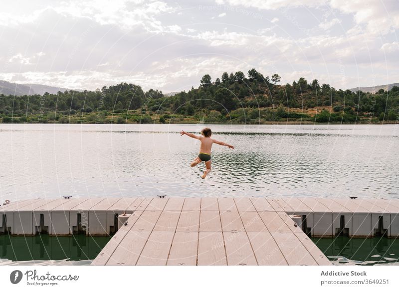 Begeisterter Junge springt vom Pier in den See springen Spaß haben Wasser Moment Kind Teich Kindheit Badebekleidung Kai hölzern Wochenende Sommer Urlaub