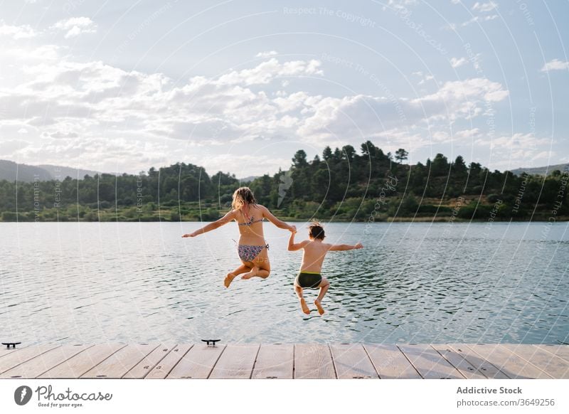 Begeisterte Geschwister springen vom Pier in den See Kinder Spaß haben Wasser Menschengruppe Geschwisterkind Moment Teich Kindheit Badebekleidung Kai hölzern