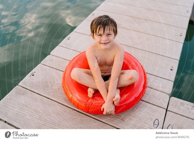 Sorgenfreier Junge auf Gummiring am Kai See Pier Kind sich[Akk] entspannen Ring Feiertag sorgenfrei Lächeln aufblasbar bezaubernd Wasser hölzern Sommer Urlaub