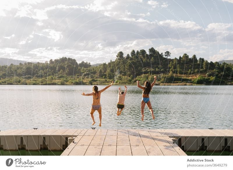 Begeisterte Geschwister springen vom Pier in den See Kinder Spaß haben Wasser Menschengruppe Geschwisterkind Moment Teich Kindheit Badebekleidung Kai hölzern