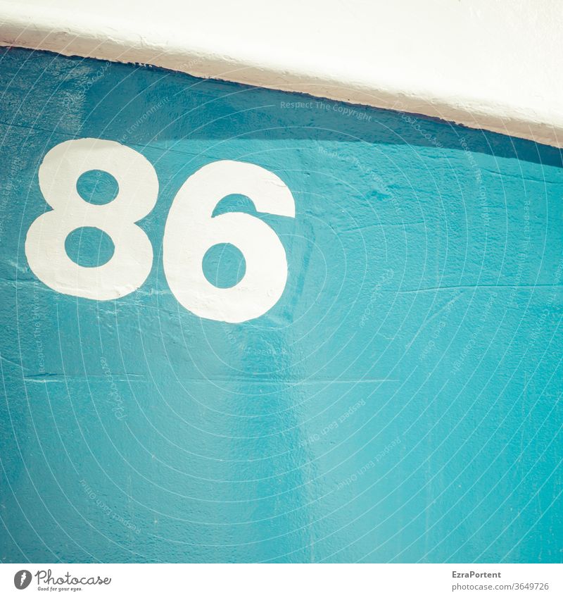 die Zahl 86 auf einer sonnenbeschienenen blauen Oberfläche mit weißen Schwung im oberen Teil der einen kecken Schatten wirft Ziffern & Zahlen Zeichen