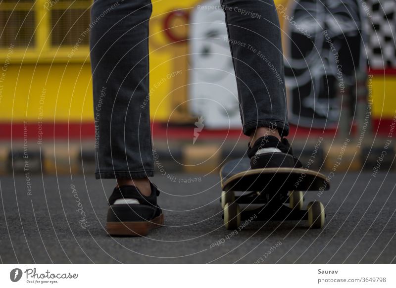 Ein junger Mann steht, während er seinen Fuß auf einem Skateboard hält. Skateboarding Sommer neue Normale Sport Freizeit Lifestyle Turnschuh im Freien
