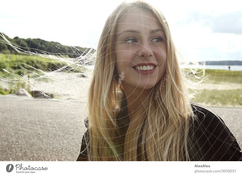 Gegenlicht Portrait einer jungen, blonden, lächelnden Frau am Meer junge Frau schön schlank langhaarig windig ästhetisch Sommer Ausflug Schönes Wetter Model