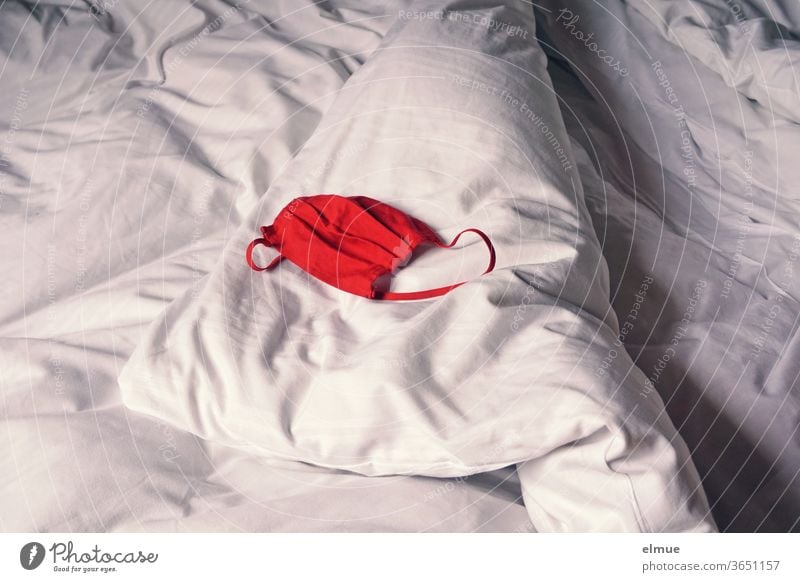 eine rote Mund-Nasen-Maske liegt auf einem weiß bezogenen Hotelbett Mundschutzmaske Bett Prävention ablegen abnehmen Nasen-Mundschutz-Maske entledigen absetzen