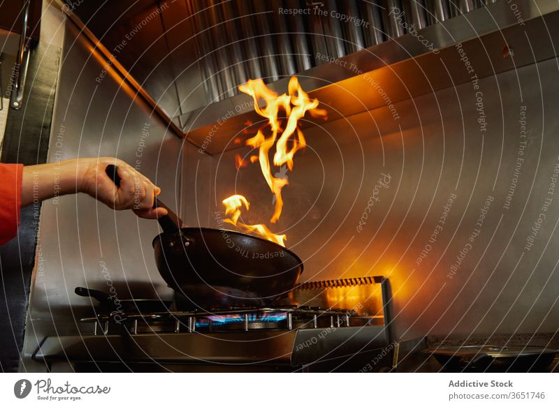 Anonymer Küchenchef entflammt Essen in der Pfanne auf dem Gasherd flambieren Lebensmittel Koch Prozess Feuer braten Hand Restaurant kulinarisch Körperteil