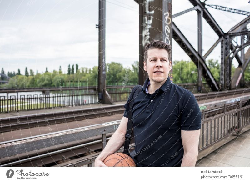 Mann mit Basketball posiert in der Nähe von Eisenbahnschienen Brücke Kaukasier Frankfurt am Main Deutschland urban Erwachsener gutaussehend Model eine Person