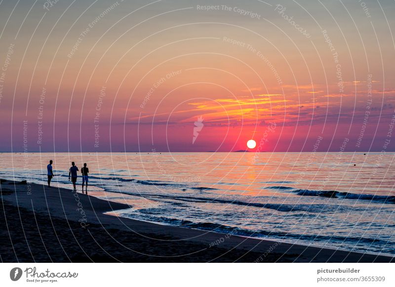 Drei Personen beobachten den Sonnenaufgang Morgendämmerung Sonnenuntergang Strand Meer drei Himmel Wolken Horizont Farbfoto Sommer Wellen Wasser rot zuschauen