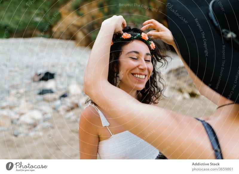 Unerkennbare Frau, die ein Diadem auf den Kopf ihrer Freundin setzt ausrichten Blume Strand Augen geschlossen sinnlich lgbt schließen Liebe lesbisch