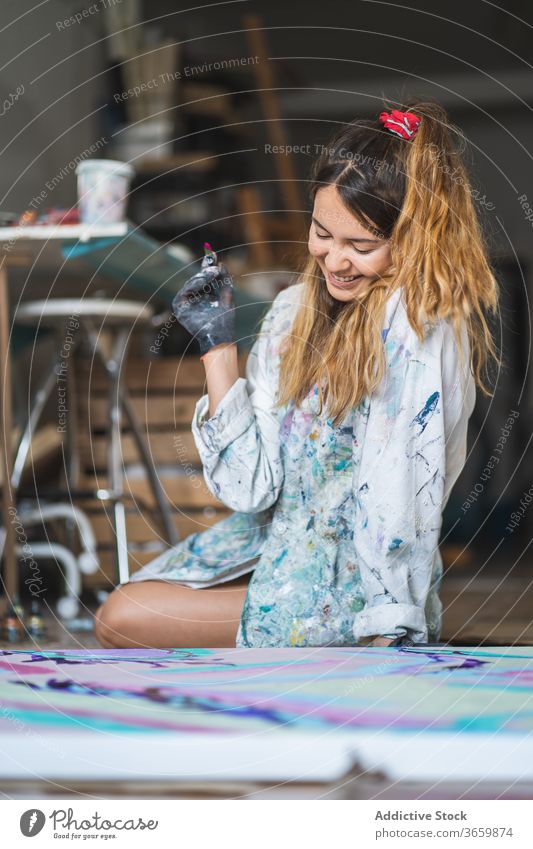 Fröhliche Malerin lacht beim Betrachten eines farbenfrohen Bildes Anstreicher Kunst Lachen Handwerk Talent liquide Barfuß Handschuh Werkstatt Künstler Papier