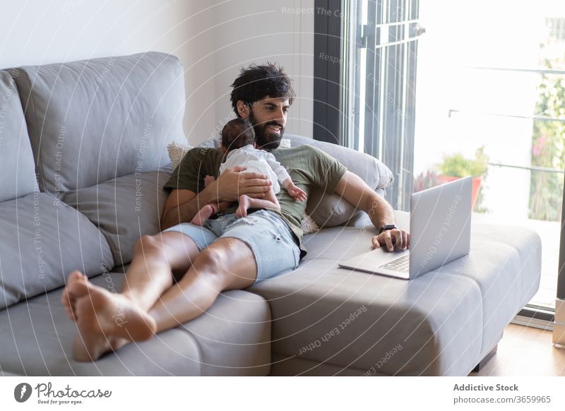Beschäftigter Vater mit Kleinkind benutzt Laptop Baby Arbeit freiberuflich Sofa beschäftigt neugeboren Projekt benutzend männlich Vaterschaft Netbook heimwärts