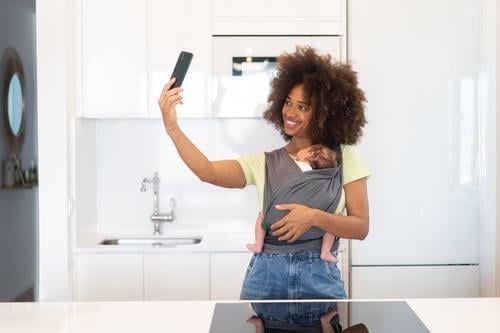 Afroamerikanische Mutter, die Selbsthilfe mit ihrem Baby nimmt schlafen Babytragetuch Selfie Liebe Smartphone heimwärts führen benutzend Frau ethnisch schwarz