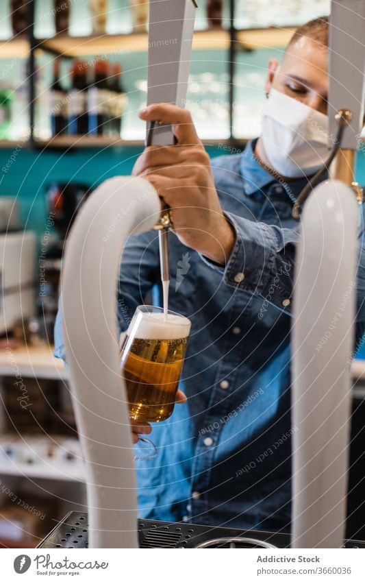Junger Mann füllt Glas mit Bier für Kunde eingießen Wasserhahn frisch Barkeeper Mundschutz Pub Tiefgang Alkohol trinken Arbeit männlich jung Hemd positiv