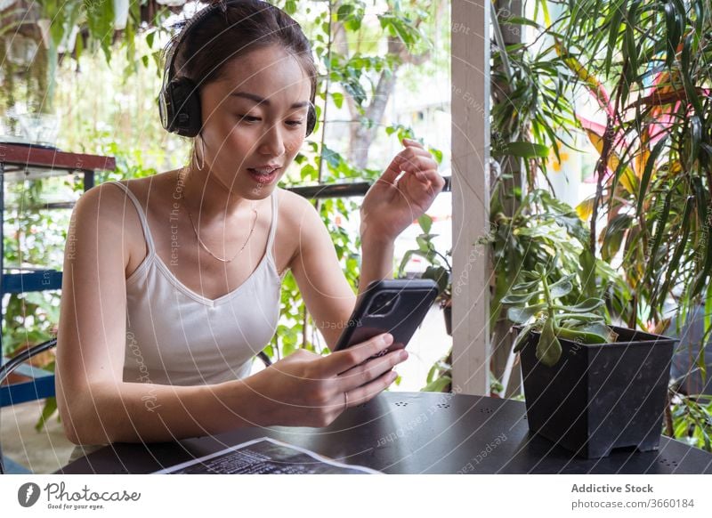 Asiatische Frau sieht Video auf Smartphone zuschauen lustig Kopfhörer genießen unterhalten benutzend Lächeln asiatisch ethnisch Sommer Apparatur jung Gerät