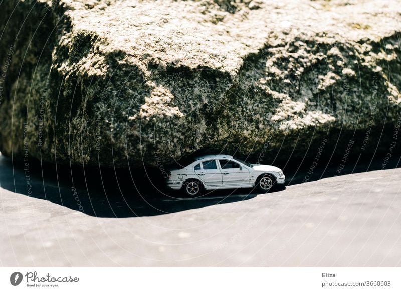 Ein Auto unterm Felsen Fahrzeug Sonne Schatten eingeklemmt gefährlich karg weiß bedrohlich Notlage Spielzeugauto PKW Panne Parken Parkplatz Verkehrsmittel Natur