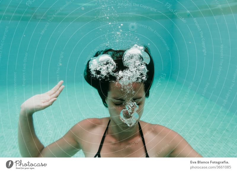 junge Frau, die in einem Schwimmbad unter Wasser taucht. Sommer und lustiger Lebensstil Schwimmsport Blasen Spaß Kaukasier Pool Sinkflug Lifestyle übersichtlich