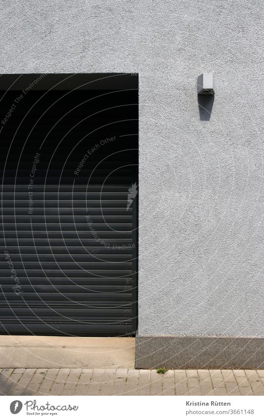 garagentor und graue fassade mit lampe hauswand rolltor mauer einfahrt strahler außenbeleuchtung gebäude architektur fassadengestaltung struktur textur schwarz