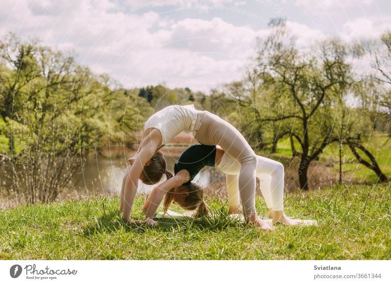 Junge Mutter und Tochter machen Yoga unter freiem Himmel im Park. Ein Mädchen und ihre Tochter führen gemeinsam Übungen durch. Das Konzept der Familie Tun Kind