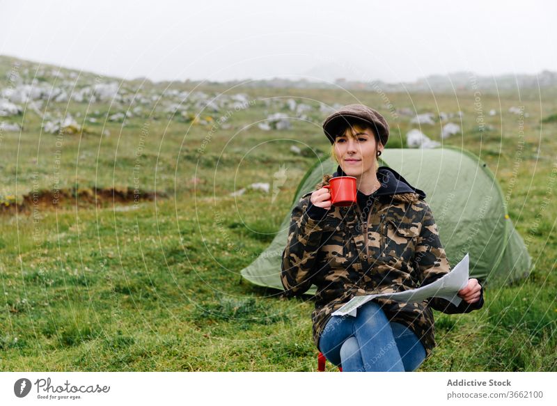 Fokussierte Frau mit Karte sitzt in der Nähe des Zeltcamps in der Natur Lager Landkarte navigieren Abenteuer Konzentration Örtlichkeit Reisender Fernweh