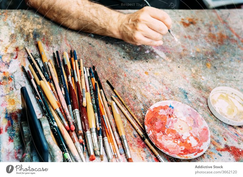 Künstlerhand mit Pinsel über der Arbeitsfläche Pinselblume Arbeitsplatte mehrfarbig Palette Farbe zeichnen kreativ Kunstwerk Beruf Pigment Hand Wasserfarbe