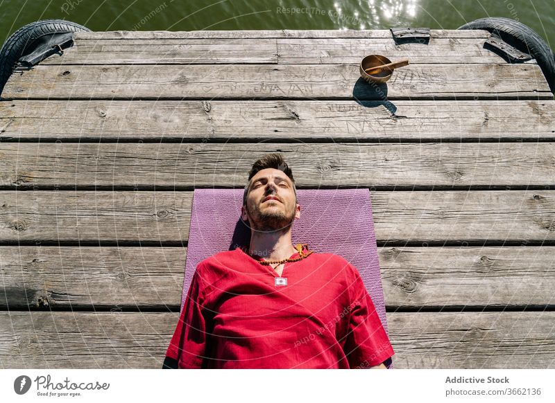 Entspannter Mann meditiert nach Yoga-Training auf Holzsteg in der Nähe der Klangschale Lügen Unterlage meditieren sich[Akk] entspannen hölzern Stauanlage