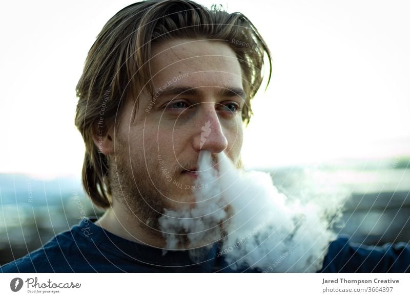 Ein junger Mann schnäuzt sich Rauch aus der Nase. Raps Jugendkultur Zigarette Rauchen Erwachsene Jugendliche Zigarettenrauch Rauch-Trick