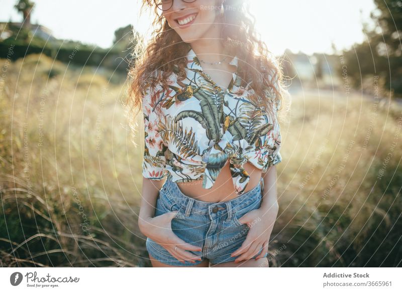 Erntefreudige Frau mit Brille steht im Sommer auf dem Feld Hand an der Hüfte Glück Schönheit Gras Lifestyle idyllisch feminin Sommerzeit Zahnfarbenes Lächeln