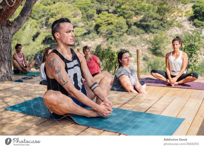 Gruppe multiethnischer Menschen, die beim Üben von Schmetterlings-Yoga-Asanas die Beine strecken baddha konasana Dehnung Klasse Lager Park Konzentration