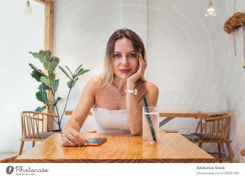 Lächelnde junge Frau sitzt am Tisch im Café ruhen trinken in die Kamera schauen positiv Top lässig sich[Akk] entspannen Getränk Freizeit Dame Blondine heiter