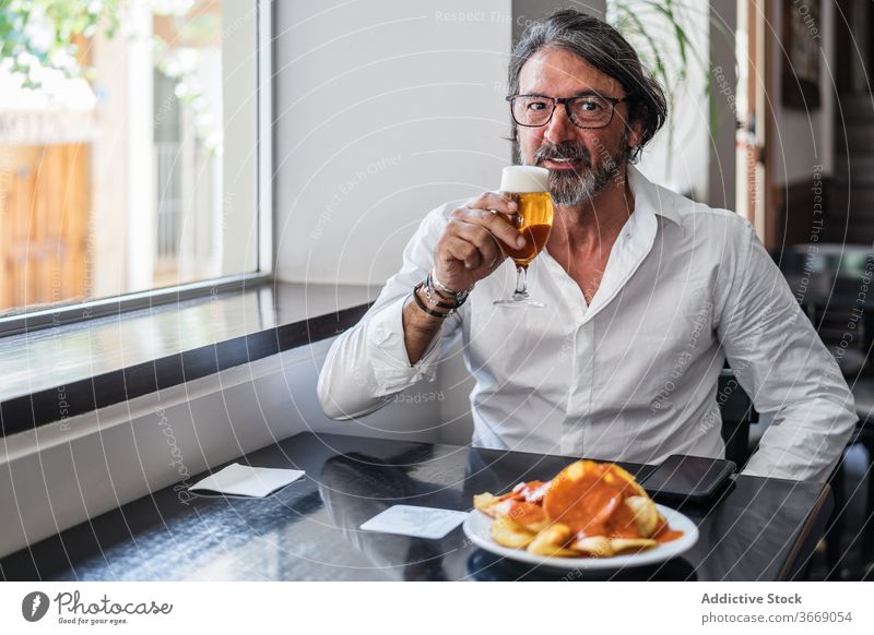 Bärtiger ethnischer Mann isst köstliches Mittagessen im Restaurant älter Café Glas Bier reif trinken positiv männlich ruhen Lächeln gealtert