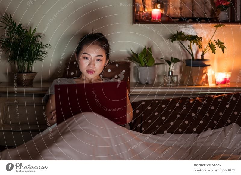 Asiatische Frau sitzt im Bett mit Laptop in der Nacht sich[Akk] entspannen Internet Komfort heimisch sitzen benutzend Gerät Apparatur Netbook genießen