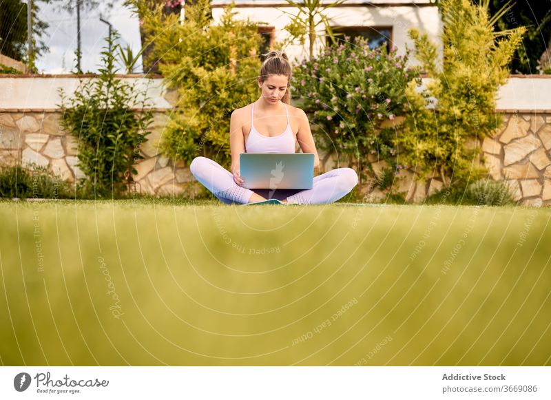 Ruhige Frau mit Laptop auf Matte im Innenhof online Tutorial Yoga wählen pflücken ruhig Sportbekleidung benutzend Unterlage Barfuß Windstille Wellness