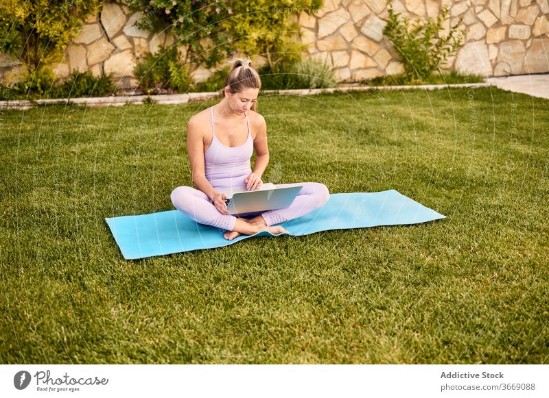 Ruhige Frau mit Laptop auf Matte im Innenhof online Tutorial Yoga wählen pflücken ruhig Sportbekleidung benutzend Unterlage Barfuß Windstille Wellness