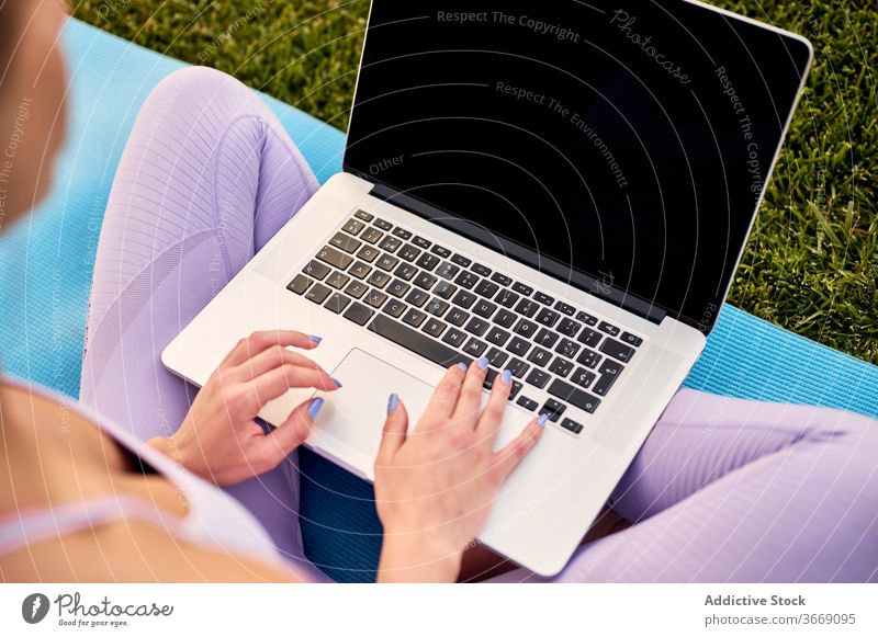 Crop anonyme weibliche Suche nach Online-Yoga-Lektion auf Laptop auf Matte online Netzwerk Beine gekreuzt Keyboard Unterlage benutzend Apparatur Gerät Netbook