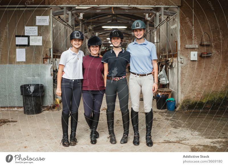 Gesellschaft von Jockeys im Stall Reiterin Frauen Zusammensein Umarmung Lächeln Porträt Pferdestall freundlich Uniform Scheune pferdeähnlich jung Menschengruppe