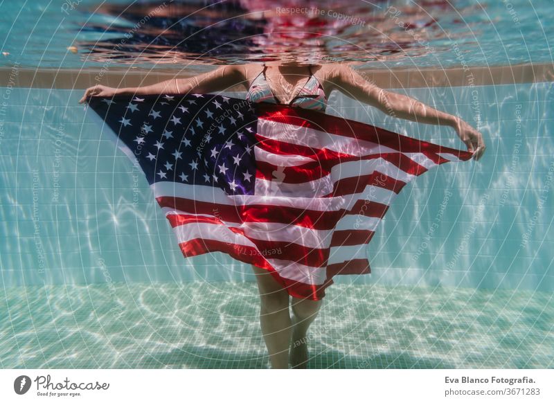 junge Frau in einem Pool, die die amerikanische Flagge unter Wasser hält. Konzept für den Unabhängigkeitstag am 4. Juli. Sommerzeit Stars and Stripes
