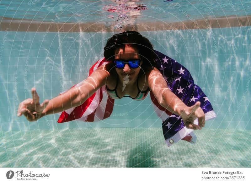junge Frau in einem Pool, die die amerikanische Flagge unter Wasser hält. Konzept für den Unabhängigkeitstag am 4. Juli. Sommerzeit Stars and Stripes