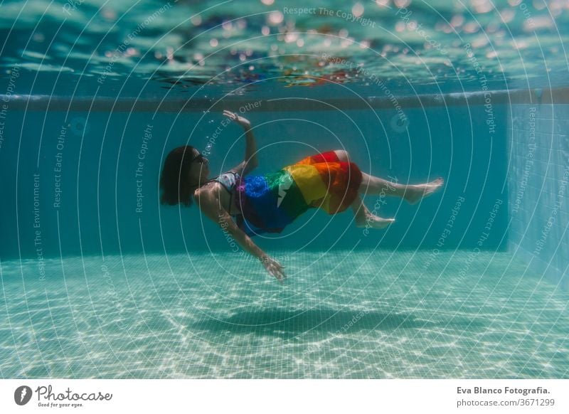 junge Frau in einem Pool, die unter Wasser eine Regenbogenflagge mit schwuler Flagge hält.LGBTQ-Konzept. Sommerzeit Schwimmbad Schwulenflagge lgbtq Beteiligung