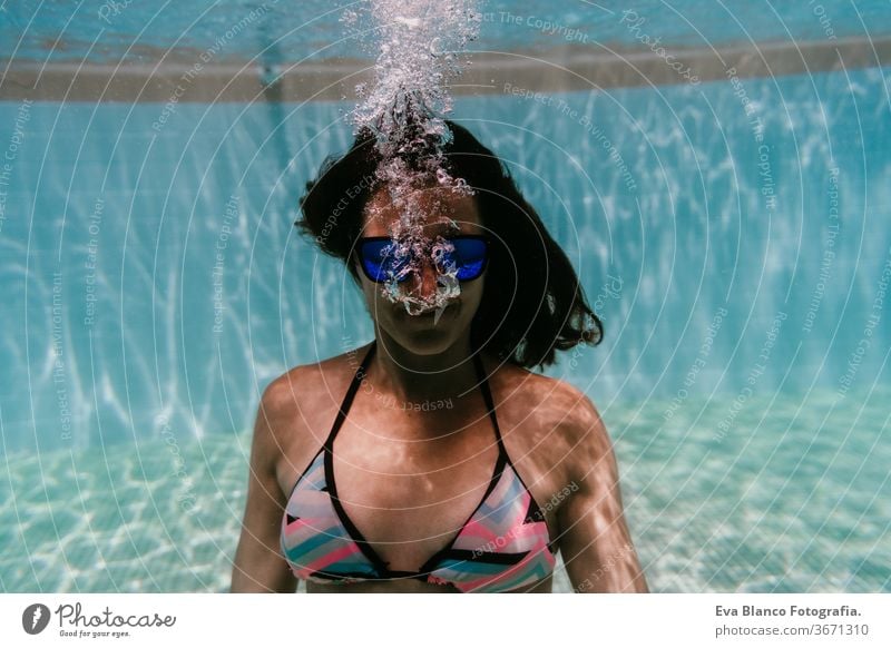 junge Frau, die in einem Schwimmbad unter Wasser taucht. Sommer und lustiger Lebensstil Sonnenbrille Schwimmsport Blasen Spaß Kaukasier Pool Sinkflug Lifestyle