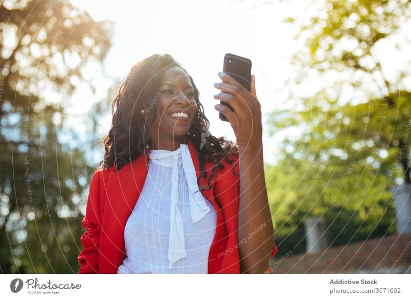 Schwarze Frau mit Smartphone Stil Bekleidung Mode traumhaft Park benutzend Handy Apparatur Gerät Funktelefon Glamour Kuss gestikulieren rot elegant farbenfroh