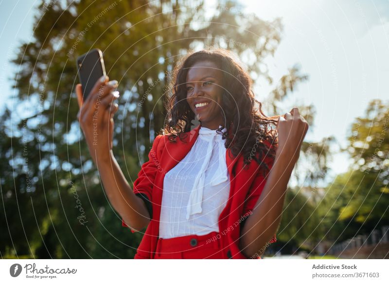 Schwarze Frau mit Smartphone Stil Bekleidung Mode traumhaft Park benutzend Handy Apparatur Gerät Funktelefon Glamour Kuss gestikulieren rot elegant farbenfroh