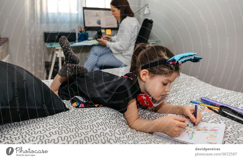 Mädchen zeichnet verkleidet, während ihre Mutter Telearbeit leistet Heimarbeitsplatz Vereinbarkeit von Beruf und Familie Schlafzimmer covid-19 Färbung