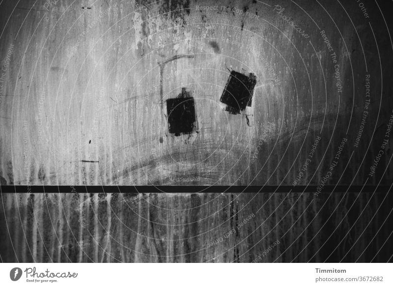 Schwarzweißfoto einer bekümmert scheinenden Wand schwarz grau Linien Spuren Rechtecke traurig Menschenleer abstrakt Gesicht