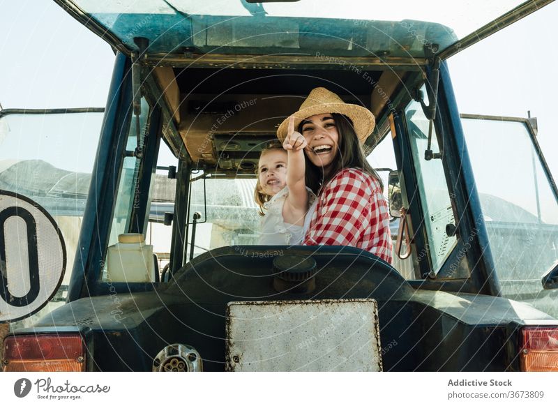 Glückliche Frau umarmt kleines Kind sitzt in Traktor auf dem Lande Mutter Umarmen Tochter Kinderbetreuung Zuneigung Punkt Finger Bonden Landschaft