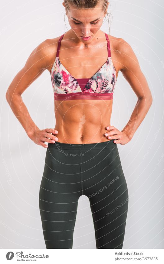 Crop schlanke müde Sportlerin in aktive Kleidung mit Pause drinnen zeigen Unterleib Sixpack Gesundheit Wohlbefinden Hand auf der Taille Sportbekleidung Bauch